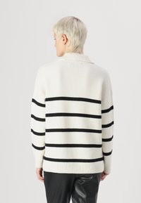 Sweter w paski w kremowym kolorze z czarnymi poziomymi paskami, wykonany z prążkowanej tkaniny. Posiada wysoki kołnierz i długie rękawy oraz luźny krój.