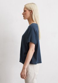 Navyblaues Kurzarmoberteil mit lockerem Schnitt und Rundhalsausschnitt, aus weichem Stoff; getragen mit hellen Hosen.