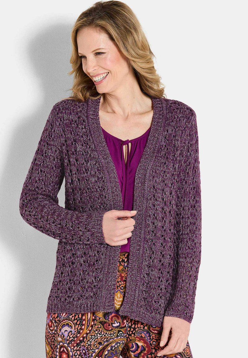 Cardigan aperto in pizzo con maniche lunghe di colore viola profondo, con un motivo testurizzato, abbinato a una maglietta viola e pantaloni a fantasia.