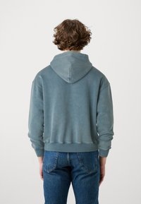 Felpa in misto cotone di un blu sbiadito con orlo doppio cucito, tasca a marsupio e cappuccio regolabile con cordino. Indossata con jeans in denim.