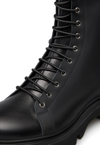 Stivale in pelle nera con lacci, soffice altezza, punta rotonda, finitura testurizzata, occhielli in metallo e lacci lisci, dotato di una suola in gomma spessa.