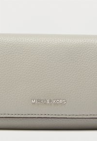 Γκρι δερμάτινο πορτοφόλι με υφή στην επιφάνεια, διακριτικές ραφές και ασημένιο ανάγλυφο λογότυπο στο μπροστινό μέρος. Компактный и прямоугольный дизайн.