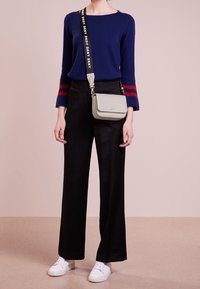 Navy sininen neule, jossa punaiset raidat, mustat leveälahkeiset housut ja vaaleanharmaa crossbody-laukku, jossa logokiristys; valkoiset tennarit viimeistelevät asun.