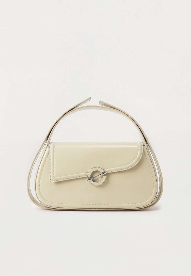 Sac à main en cuir crème avec rabat incurvé, fermoir circulaire en argent et poignée courte sur le dessus, sur fond blanc uni.