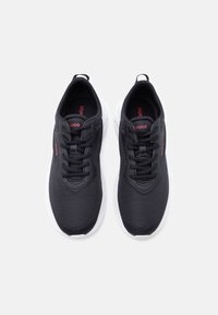 Paire de baskets noires avec dessus en tissu texturé, lacets noirs, semelles blanches et marquage rouge "HUGO" sur les languettes et les côtés.