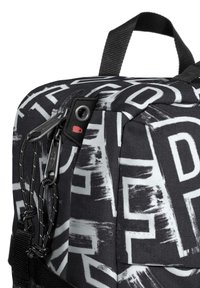 Svart och vit zip-fodrad ryggsäck med ett graffiti-liknande mönster, texturerat tyg och hårdvarudetaljer med en röd accent.