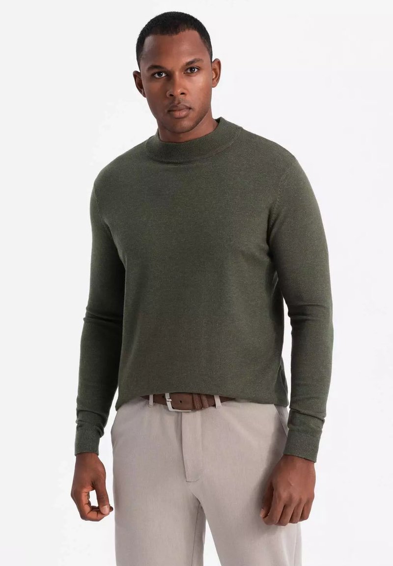 Groen gebreide trui met een hoge kraag, lange mouwen en een ontspannen pasvorm, gecombineerd met lichte broek.