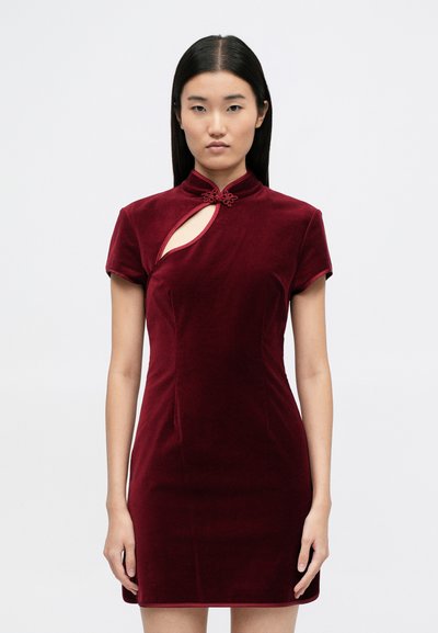 Rochie din catifea burgundy, cu maneci scurte, având un guler înalt, decupaj în formă de cheie și un detaliu decorativ sub formă de nod la decolteu.