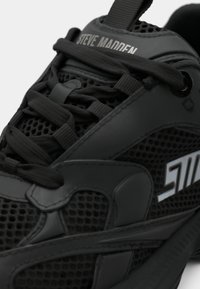Close-up of black Steve Madden sneaker featuring mesh fabric, thick laces, and a logo patch on the side.
