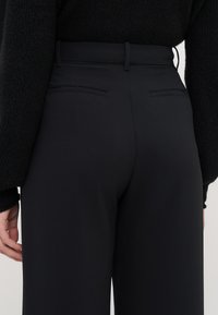 Černé elegantní kalhoty s hladkým materiálem, vysokým pasem, poutky na opasek a dvěma zadními kapsami s čistým designem.