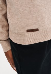 Beżowy sweter wykonany z miękkiego materiału z prążkowanymi mankietami i dołem. Posiada brązową metkę z napisem "blue shadow" na dole.