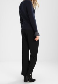 Námořnický pletený svetr s šedými rozšířenými rukávy v kombinaci s černými širokými kalhotami a černými vysokými kotníkovými botami.