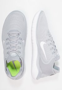 Jasnoszare buty sportowe z fakturowaną cholewką, białymi detalami i jaskrawozielonym wnętrzem. Posiadają okrągłe sznurowadła oraz amortyzowaną podeszwę.