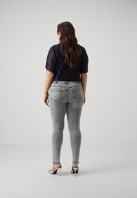 Vaqueros ajustados grises con un acabado desgastado, cintura alta y bolsillos traseros, combinados con una blusa de talle alto azul marino y zapatos de tacón plateados.