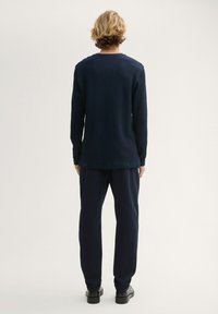 Granatowa koszula z długim rękawem z teksturowanej tkaniny, w połączeniu z dopasowanymi spodniami. Ubranie charakteryzuje się luźnym krojem i prostym designem, bez widocznych wzorów.