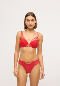 Ensemble de lingerie en dentelle rouge comprenant un soutien-gorge structuré avec des détails à lanières et des éléments en or, accompagné d'un string assorti. Motif floral texturé.