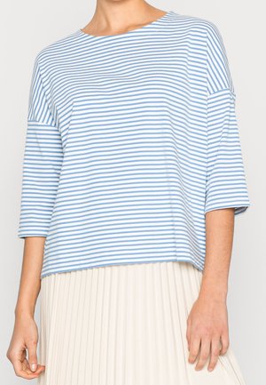 Personne portant une chemise à rayures horizontales bleu clair et blanc avec des manches trois-quarts et une jupe plissée blanche.