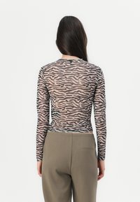 Langemouwen, doorschijnende top in een bruin en zwart zebra print, geknoopt in de taille. Gecombineerd met hoge, loose-fitting olijfgroene broeken.