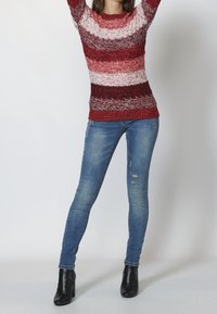 Czerwono-biały sweter w paski z teksturowanym wykończeniem, zestawiony z postrzępionymi niebieskimi rurkami i czarnymi botkami za kostkę.