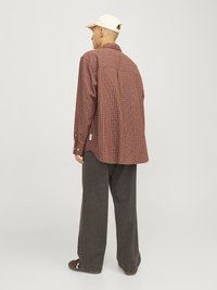 Chemise à manches longues à carreaux dans des nuances de marron et de rouille, coupe décontractée, détail de l'empiècement au dos, associée à un pantalon large gris et une casquette crème.