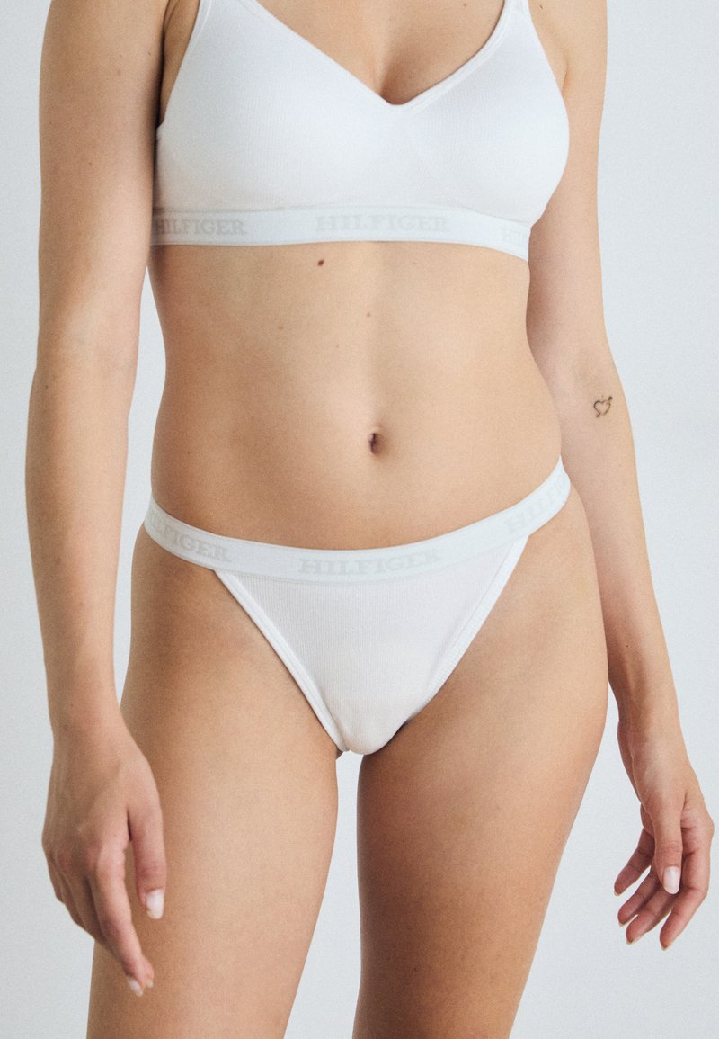 Ensemble bralette et string en coton blanc avec une texture côtelée et une ceinture portant le logo "HILFIGER" en gris. Design simple et classique.