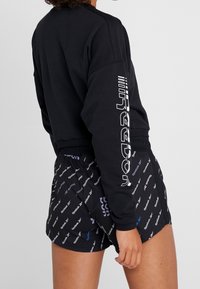 Felpa nera con testo bianco sulla manica e pantaloni corti neri con un motivo di logo ripetuto in bianco e blu. Tessuto morbido, vestibilità rilassata.