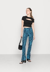 Top preto cropped com detalhe recortado, combinado com calças azuis de cintura alta com um padrão ondulado, e sandálias pretas de salto bloco.