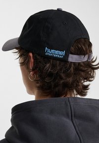 Svart keps med grå skärm, med blå broderad "hummel SPORTSWEAR" text på bakremmen. Texturerat material, justerbar passform.