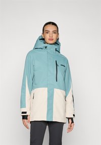 Teal and cream waterproof jacket with a zippered pocket, adjustable hood, and elastic cuffs. Features contrasting color blocking.