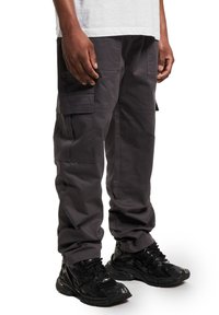 Pantalones cargo gris oscuro hechos de tela resistente, con múltiples bolsillos, un corte relajado y combinados con zapatillas negras.