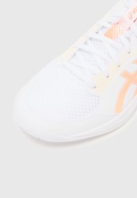 Weißer Sportschuh mit strukturiertem Mesh-Obermaterial, ausgestattet mit leichten orangefarbenen Akzenten und einem kontrastierenden Markenlogo an der Seite.