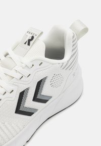 Hvid atletiksko med sorte chevron-logoer på siden, mesh-overdel, polstret krave, snørebånd og trækstrop på hælen.