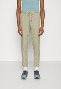 Ljusbeige cargobyxor med dragsko i midjan, sidofickor och elastiska muddar, kombinerat med blå träningsskor och vita strumpor.