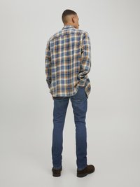 Long-sleeve flannel shirt in blue, brown, and cream plaid pattern, paired with slim-fit blue jeans and dark brown shoes.