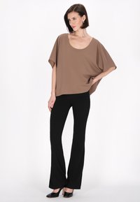 Brun batwing kortærmet top med scoop neckline, parret med tætsiddende sorte flarebukser og sorte hæle. Glat stof med en afslappet pasform.