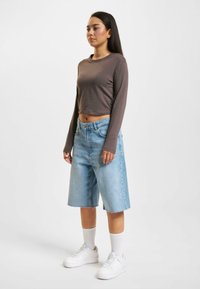 Brown cropped long-sleeve top paired with light blue denim shorts, featuring a relaxed fit, frayed hem, and white sneakers with crew socks.