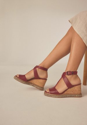 Burgunderfarbene Leder-Wedgesandalen mit Korkbasis, mit einem Kreuzdesign und Riemen um den Knöchel. Geflochtene Akzente um die Sohle.
