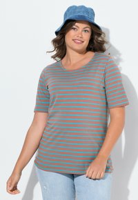 Camiseta a rayas en marrón y turquesa, de mangas cortas, con cuello redondeado y textura suave. El modelo lleva puestos unos vaqueros azul claro y un sombrero tipo cubo azul.