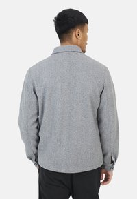 Grijze wollen blendjas met een kraag, lange mouwen en knopen bij de manchetten. Heeft een gestructureerde afwerking en een recht afgewerkte zoom.