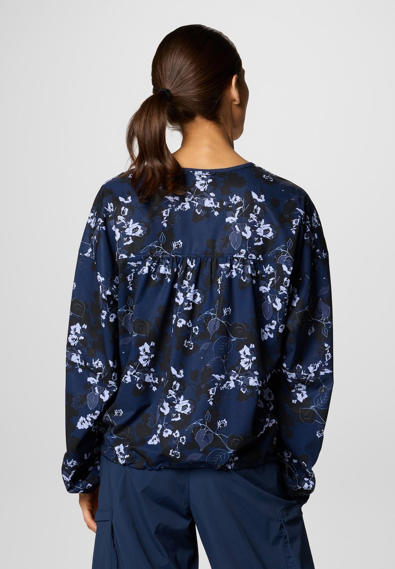 Marineblaue Bluse mit Blumenmuster, langen Ärmeln und gerafftem Rückendetail. Der Stoff wirkt glatt mit einem leichten Glanz.