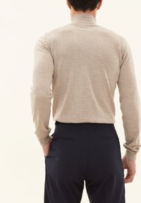 Beige langærmet turtleneck sweater med ribbede manchetter, parret med mørkeblå bukser. Glat tekstur, kropsnær pasform.