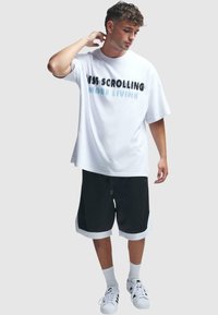 Tricou oversized alb cu text negru și albastru. Șorturi negre cu manșete albe. Stilizat cu adidași albi și șosete până la gleznă.