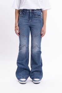 Jeans din denim albastru cu talie înaltă și picior evazat, având un design curbat al buzunarelor și zone uzate, completate cu un tricou alb și adidași.