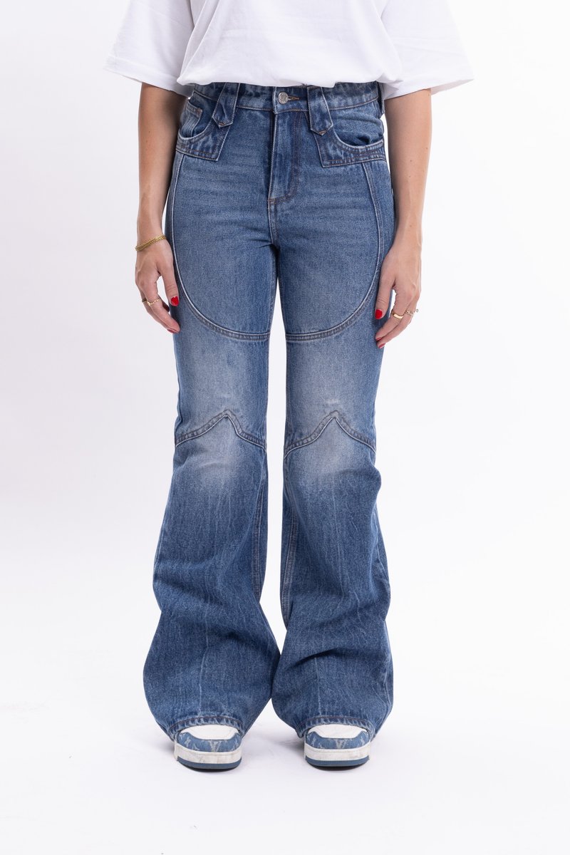 Jeans din denim albastru cu talie înaltă și picior evazat, având un design curbat al buzunarelor și zone uzate, completate cu un tricou alb și adidași.