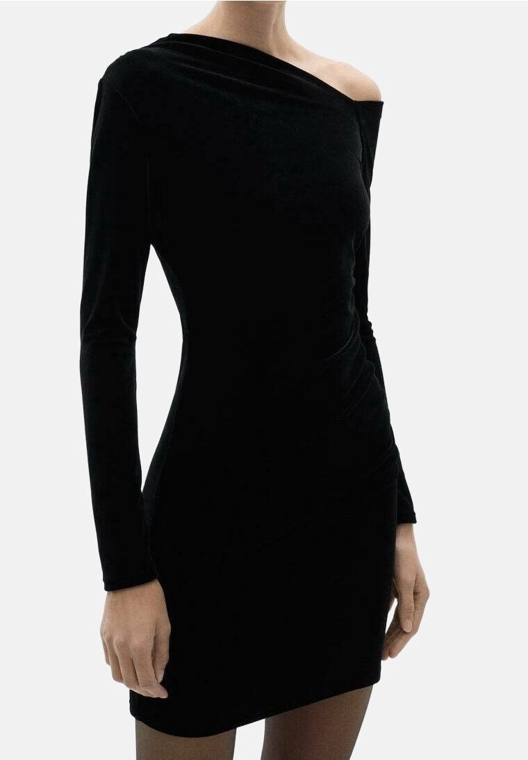 Robe noire moulante à manches longues, épaules dénudées, portée par une personne, avec un ourlet court et un léger froncement sur un côté.