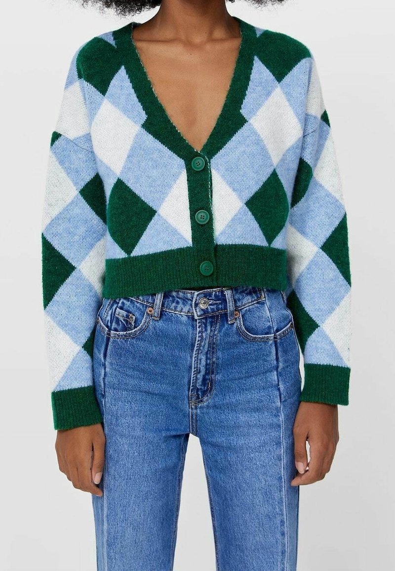 Green and blue argyle cropped cardigan with a deep V-neck and five green buttons, paired with high-waisted blue denim jeans.