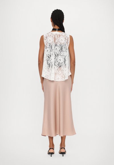 Sleeveless white lace top layered over a pink satin midi skirt, featuring a flowy design and delicate floral patterns, paired with black heels.