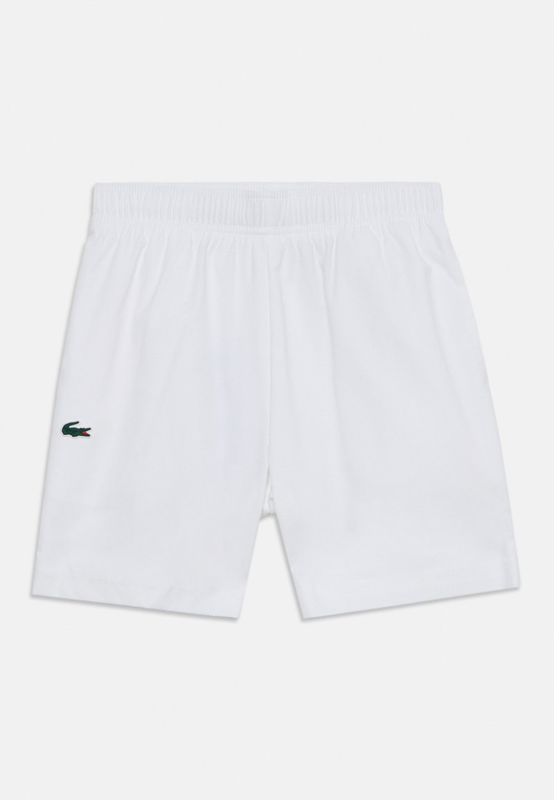 Shorts blancs à taille élastique avec un petit logo crocodile vert et rouge sur la jambe gauche sur fond uni.