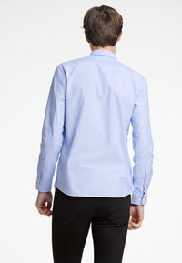 Camicia azzurra a maniche lunghe con colletto a punta, caratterizzata da una trama liscia e polsini abbottonati, indossata con pantaloni neri.