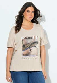 Camiseta beige de manga corta, con un gráfico de un sombrero y texto. Tela suave con un ajuste relajado y cuello redondo.